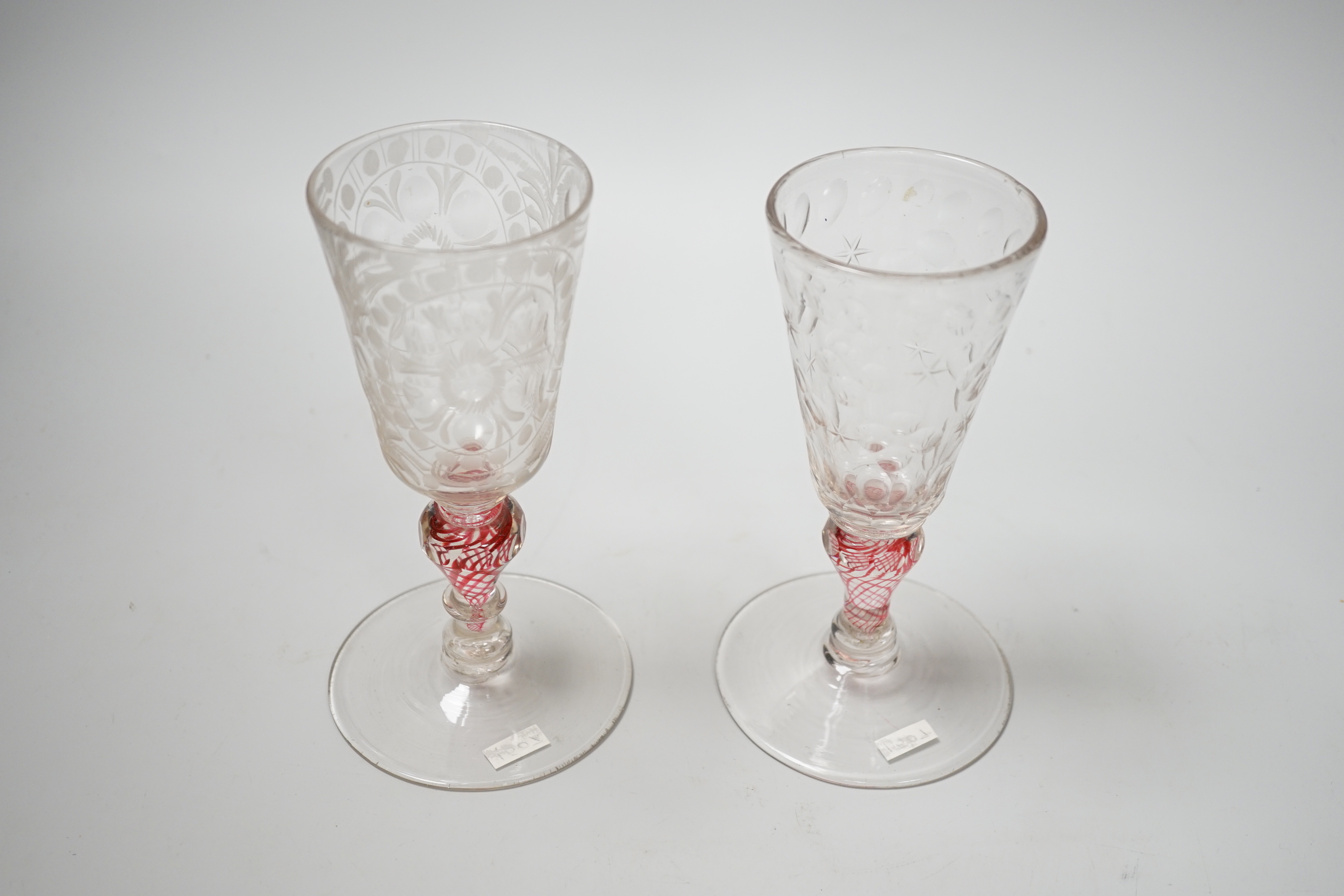 Two similar 18th century Continental goblets, both with elongated bowls heavily engraved with polished roundels, on inverted baluster stems including red colour twists and various collars, conical feet with rough pontils